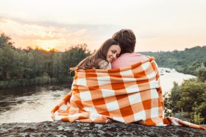An image of a couple sitting with a blanket watching a sunset
